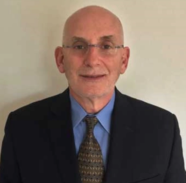 Professional headshot of bald man wearing glasses, blue shirt, and dark blazer against neutral background.