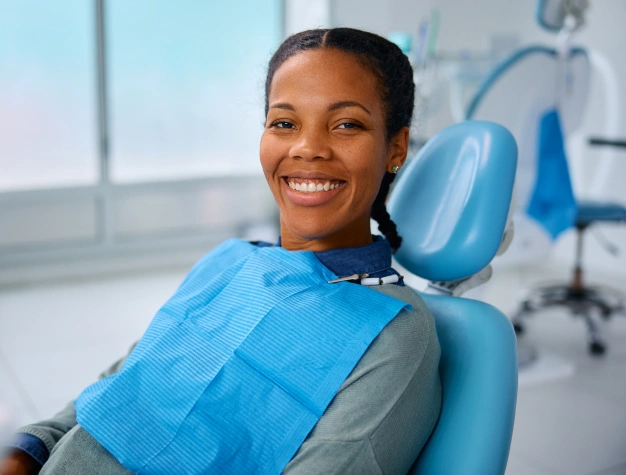 Smiling woman in dental bib sitting in blue dentist chair at modern dental office.