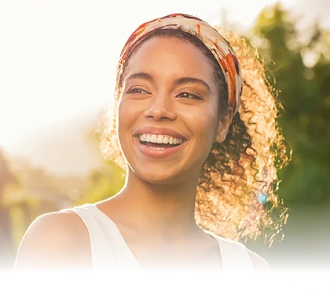 Smiling woman outdoors in natural sunlight wearing headband, promoting dental care and wellness.